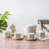 Tea set with plaid pattern on a wooden table with a plant in the background