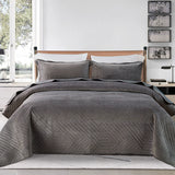 Gray quilted bedding set on a bed in a bedroom with decor elements.