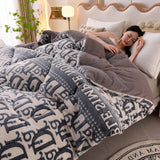 Woman lying in bed under a patterned blanket with a neutral background