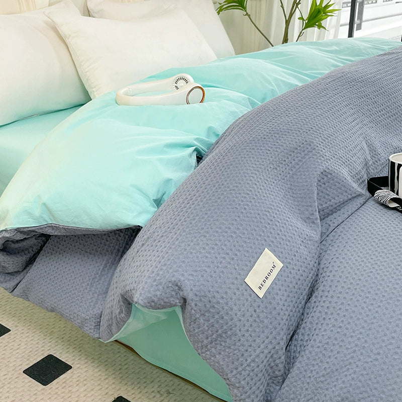 Gray textured comforter on a bed with a light blue blanket and white pillows.