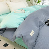 Gray textured comforter on a bed with a light blue blanket and white pillows.
