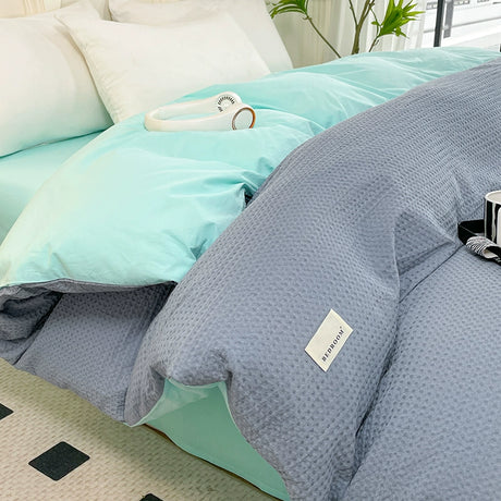 Gray textured comforter on a bed with a light blue blanket and white pillows.