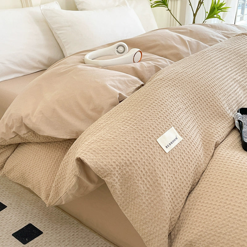 Beige textured comforter on a bed with a visible brand label.