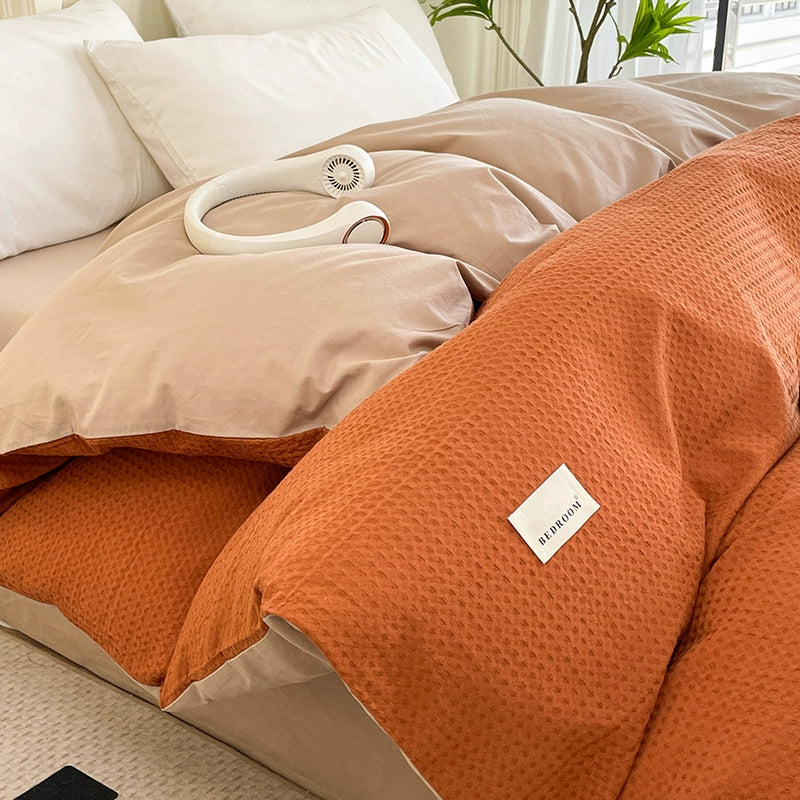 Orange textured blanket with a brand label on a bed in a bedroom setting