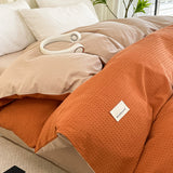 Orange textured blanket with a brand label on a bed in a bedroom setting