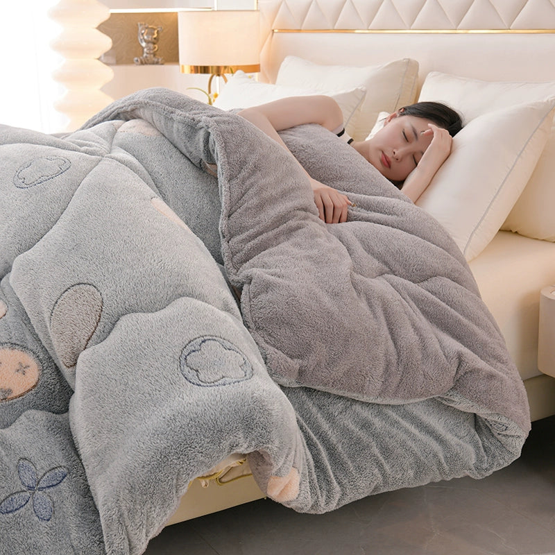 Person wrapped in a fluffy gray blanket with heart patterns on a bed.