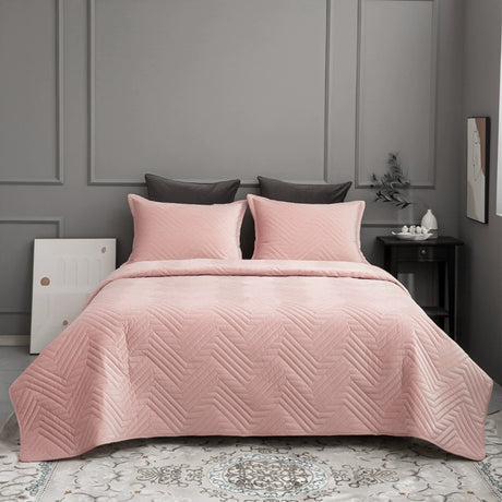 Pink quilted bedspread on a bed in a bedroom with gray walls and a nightstand.