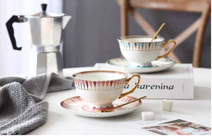Cup and saucer set with a spoon on a table with a coffee maker in the background.