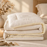 A folded beige quilted comforter with white tags attached, photographed on a clean white studio background.