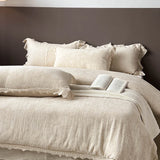Beige textured bedspread with lace details on a bed against a dark wall.