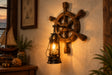 Nautical ship's wheel wall sconce with a hanging vintage-style lantern light, mounted on a plain wall with the text 'Turn on the lights' in the upper left.