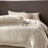 Beige textured bedspread with lace details on a bed against a dark wall.
