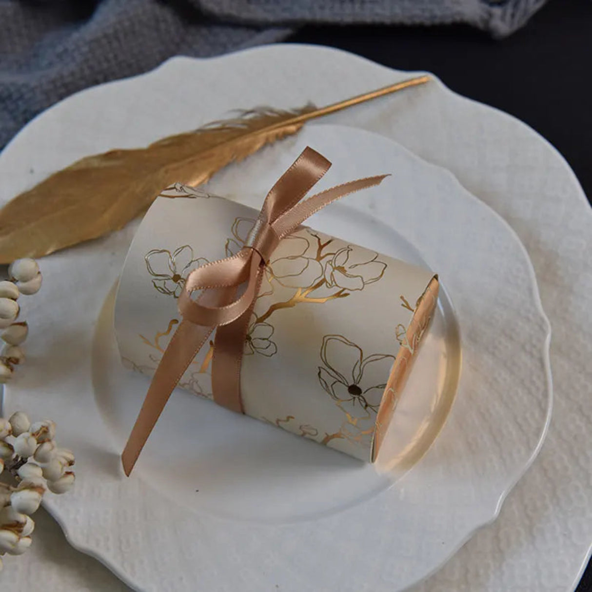 Decorative box with a gold ribbon on a white plate with a gold leaf and dried flowers.
