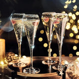 Four champagne flutes with bubbles on a dark background with festive lights