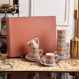 Set of colorful zigzag patterned cups and saucers on a marble surface with a pink box in the background.