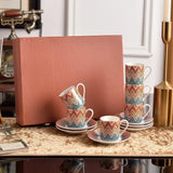 Set of colorful zigzag patterned cups and saucers on a marble surface with a pink box in the background.