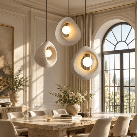 Three modern teardrop pendant lights with textured off-white stone-like outer shells and glowing warm bulbs, hanging in a stylish dining room with beige walls, striped curtains, and a large arched window.