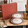 Two-tiered decorative plate set with a red box on a table.