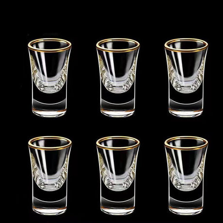 Set of six clear shot glasses with gold rims on a black background