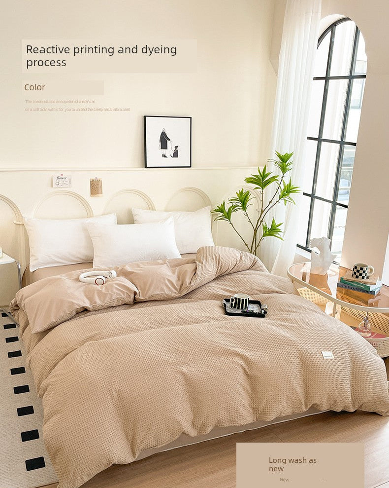 Beige bedding set on a bed with a neutral-colored wall and window in the background.