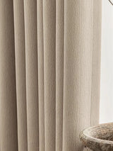 Close-up of beige textured curtains with a stone sink in the background