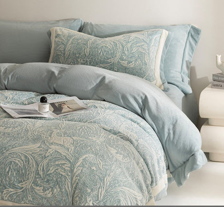 Teal patterned bedding set on a bed with pillows and a nightstand.