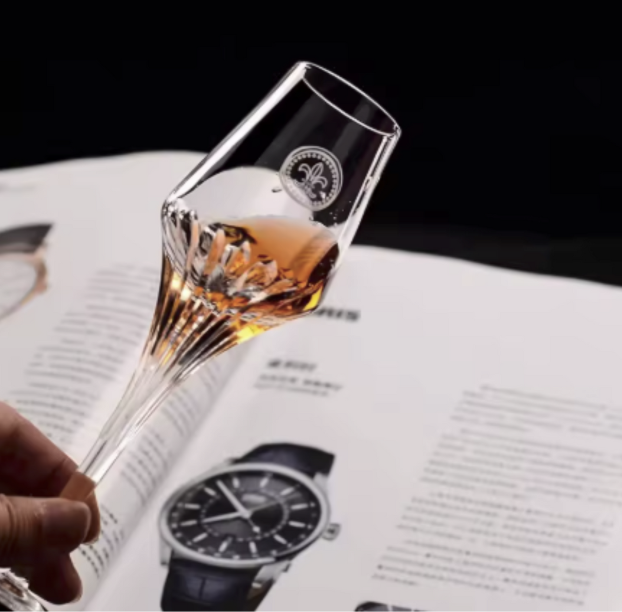 Glass with a drink held over an open book featuring a watch illustration