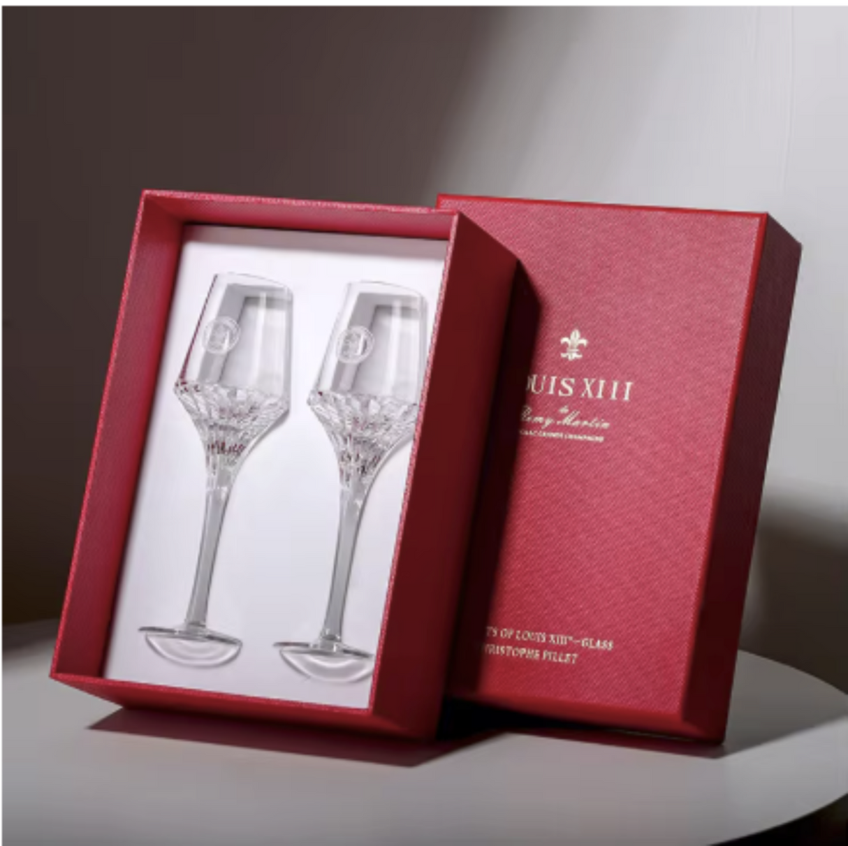 Two crystal wine glasses in a red Louis XIII box on a white surface.