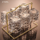 Clear glass ice cubes with a gold holder on a reflective surface.