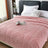 Pink blanket on a bed with pillows and a book in a bedroom setting
