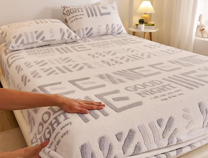 Bed with a textured blanket featuring text, hands touching the blanket, and a nightstand in the background.