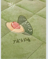 Product comparison between two versions of a green quilt with embroidered design on a light gray background.