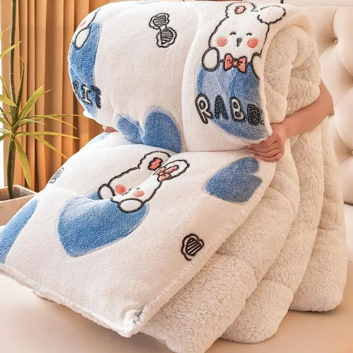 Fluffy blanket with cartoon rabbit design held by a person indoors.