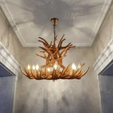 A rustic antler-style chandelier with multiple candle-style lights hanging in a hallway with textured walls and a coffered ceiling.