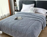 Gray textured blanket on a bed with a nightstand and pillows in a bedroom setting.