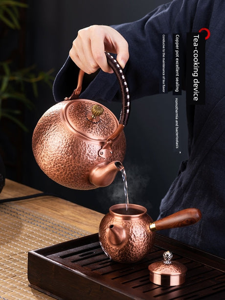 Copper teapot being used to pour tea into another copper teapot on a wooden tray.