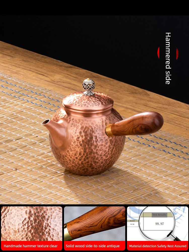 Copper teapot with wooden handle on a woven surface, showing hammered side.