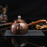 Copper teapot with wooden handle on a dark surface