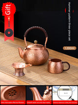 Copper tea set with teapot, cup, and strainer on a wooden surface with a dark background.