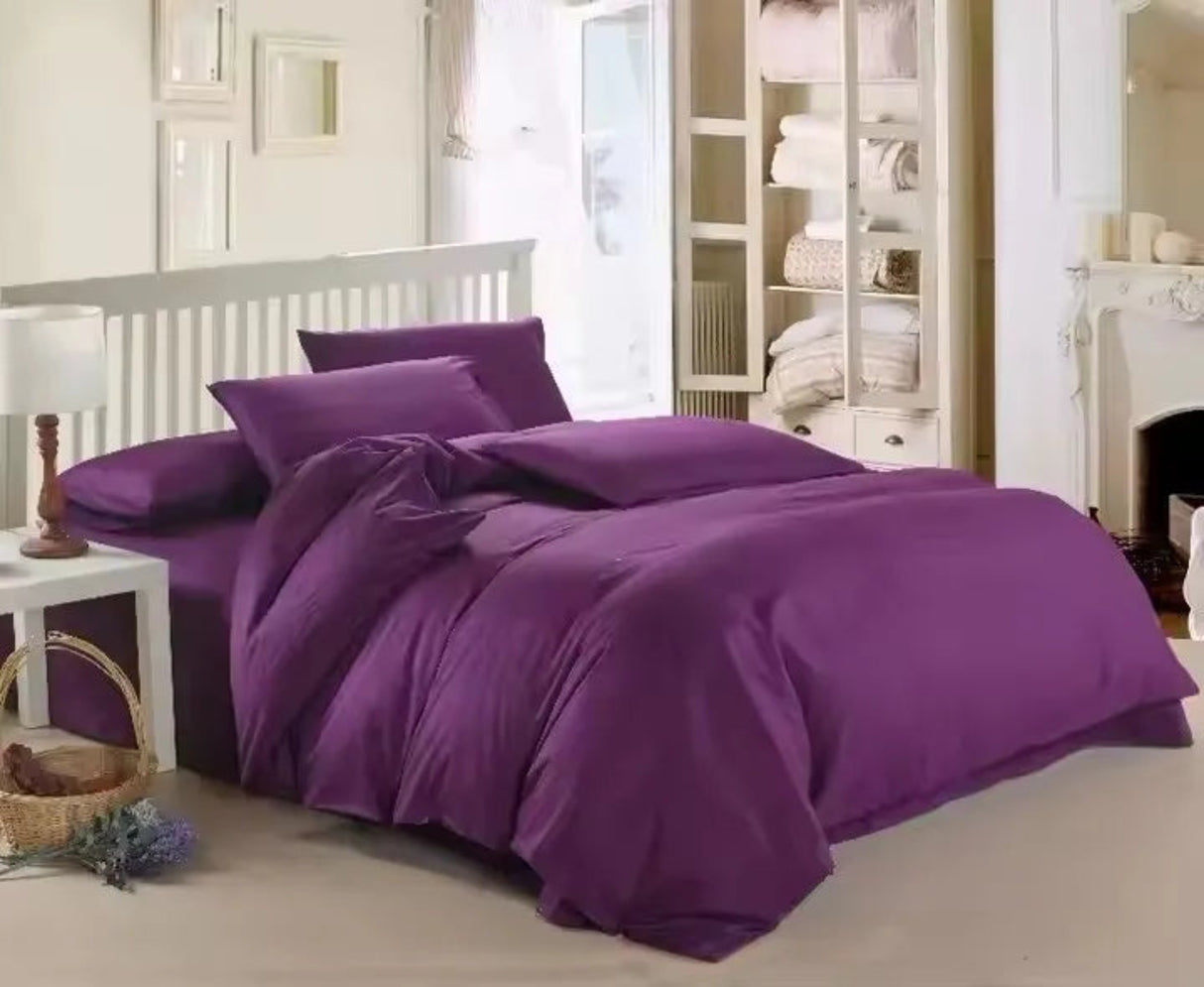 Purple bedding set on a bed in a bedroom with white walls and furniture.