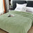 Green blanket on a bed with white pillows in a bedroom setting