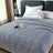 Gray textured blanket on a bed with a nightstand and pillows in a bedroom setting.