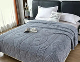 Gray textured blanket on a bed with a nightstand and pillows in a bedroom setting.