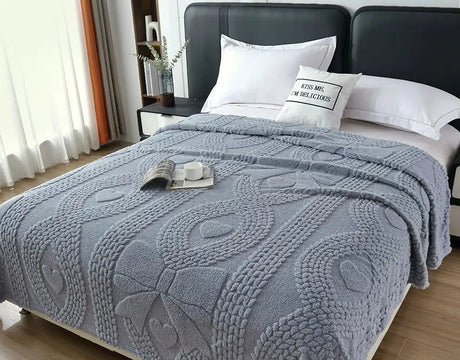 Gray textured blanket on a bed with a nightstand and pillows in a bedroom setting.
