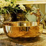 Gold ceramic sink with faucet on a marble surface, decorative mirror in the background