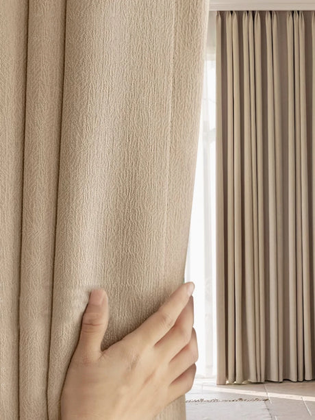 Hand opening a beige curtain to reveal light streaming in