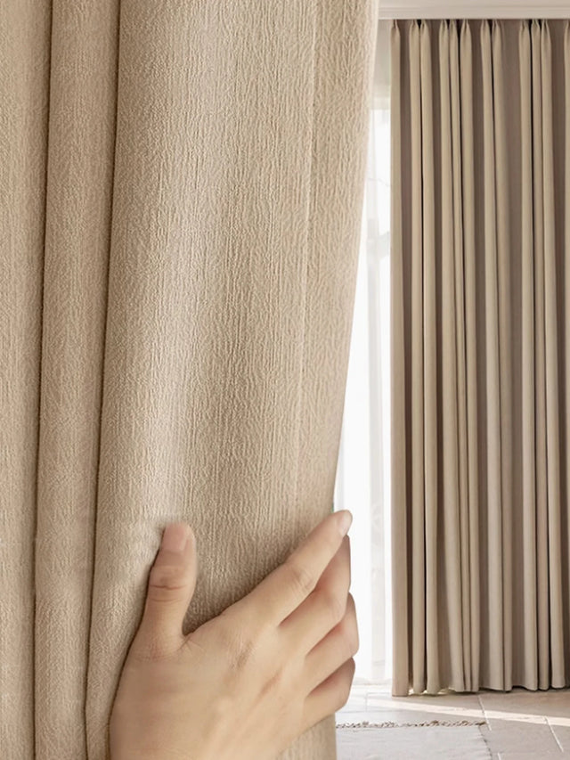 Hand opening a beige curtain to reveal light streaming in