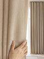 Hand opening a beige curtain to reveal light streaming in