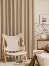 Beige chair in a living room with curtains and a side table.