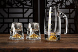 Set of clear glassware with gold accents on a wooden surface against a dark decorative wall.
